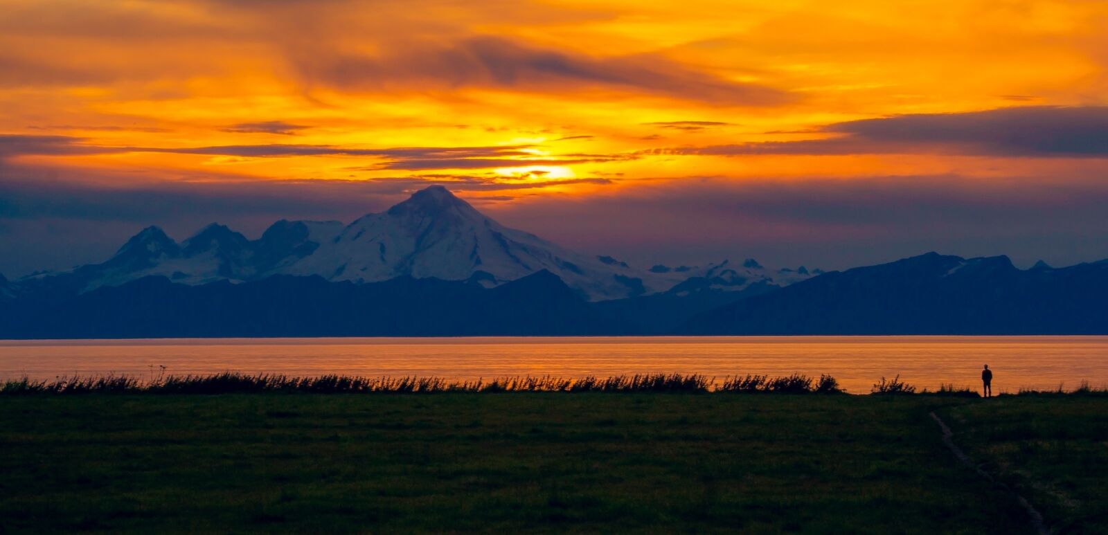 A solitary silhouette watches the sunset over Mount Iliamna in Ninilchik, Alaska. Photo by Shutterstock.