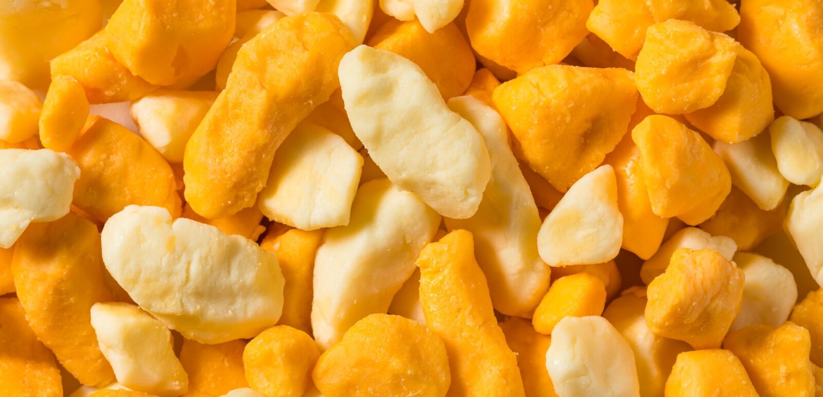 Raw organic yellow and white cheese curds in a bowl.