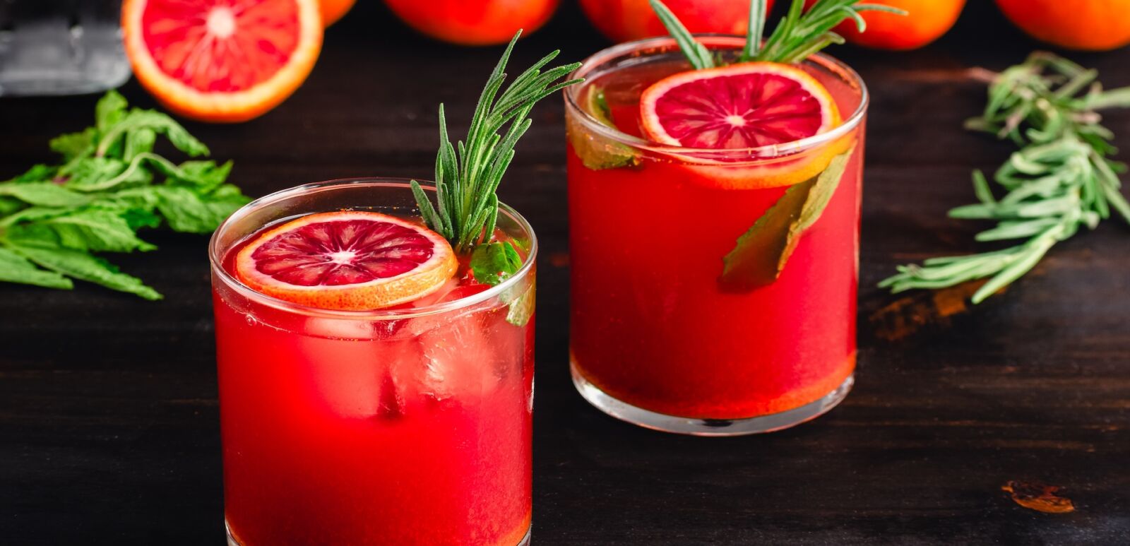 Sparkling Blood Orange Mocktails Garnished with Fresh Herbs: Mocktails with citrus juice, ginger, turmeric, rosemary, and mint in rocks glasses