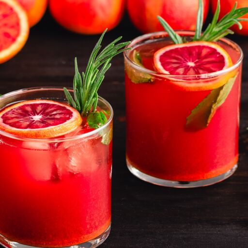 Sparkling Blood Orange Mocktails Garnished with Fresh Herbs: Mocktails with citrus juice, ginger, turmeric, rosemary, and mint in rocks glasses