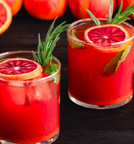 Sparkling Blood Orange Mocktails Garnished with Fresh Herbs: Mocktails with citrus juice, ginger, turmeric, rosemary, and mint in rocks glasses