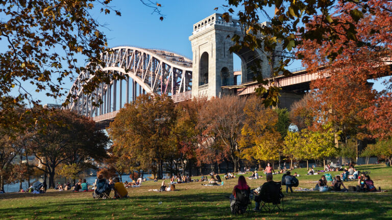 Astoria Queens, New York USA - November 8 2020: Astoria Park with the Hell Gate Bridge and a Field with People and Colorful Trees during Autumn