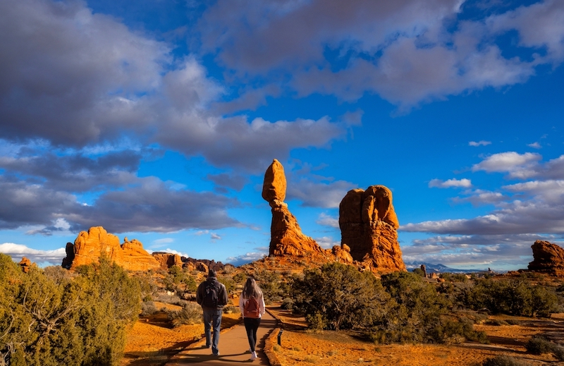 Couple hiking in red mountains. Friends walking on Balanced Rock trail.  Moab, Arches national Park, Utah. Photo via Shutterstock.