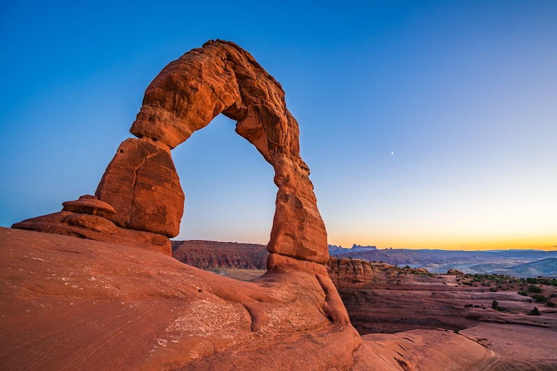 Delicate Arch - The most famous landmark of the Arches National Park in Utah after sunset in blue hour twilight. Photo via Shutterstock.