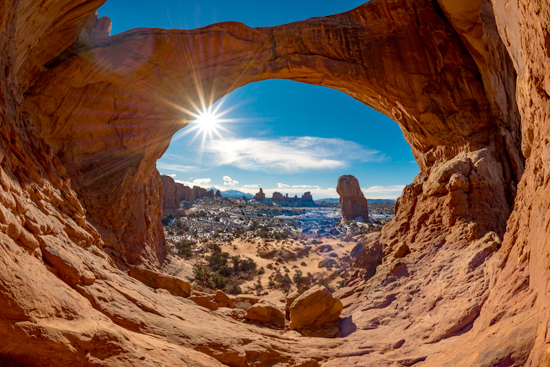 Double Arch in Moab with snow and a sun star in a blue sky. Photo via Shutterstock.